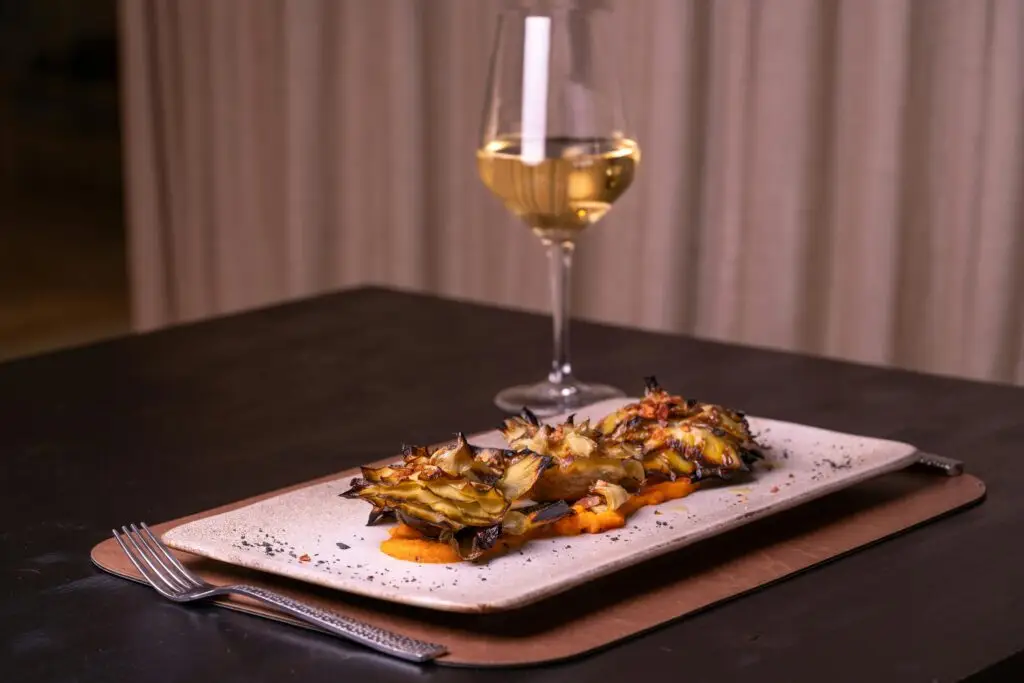 A sophisticated artichoke dish paired with a glass of white wine on a dark table.